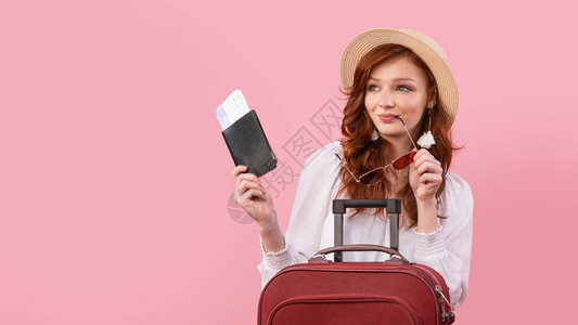 旅游女客随手提箱旅行持有护照和在粉红工作室背景上登机的旅客通行证图片