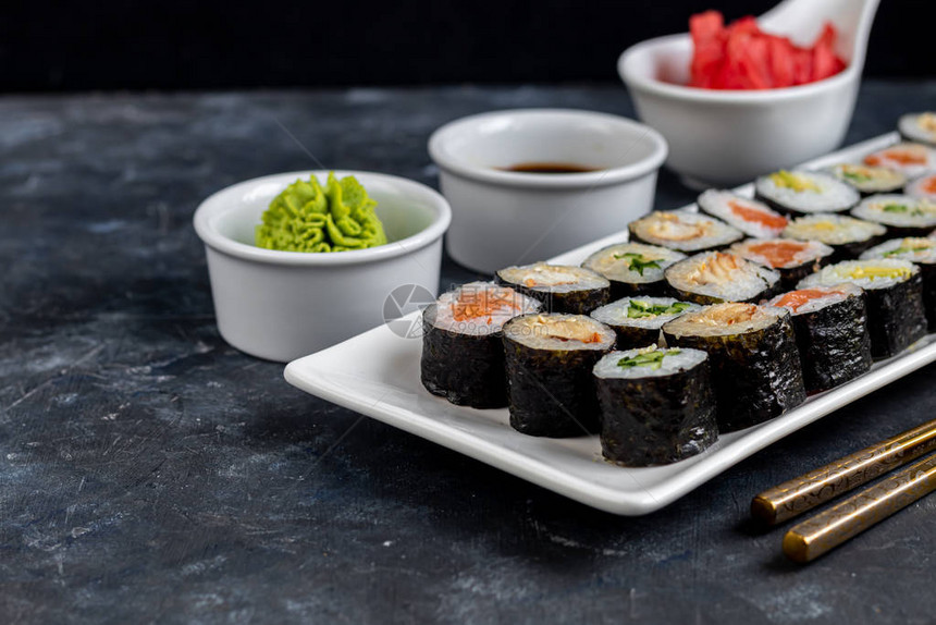 寿司配鱼鳗鱼鳄梨包裹在紫菜海藻中素食者的食物酱油生姜芥末放在白碗图片