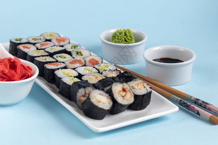 寿司配鱼黄瓜鳗鱼鳄梨包裹在紫菜海藻中素食者的食物酱油生姜芥末放在白碗图片