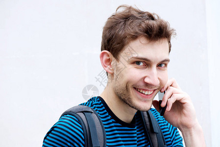 透过白色背景与手机交谈时微笑的年轻男子近距离图片