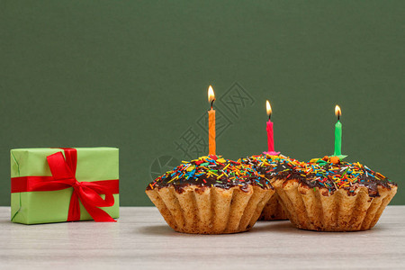 带红丝带的礼品盒和带有巧克力釉和焦糖的生日纸杯蛋糕图片