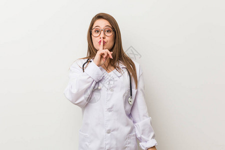 年轻女医生站在白墙上保守秘密或要求保持沉默图片