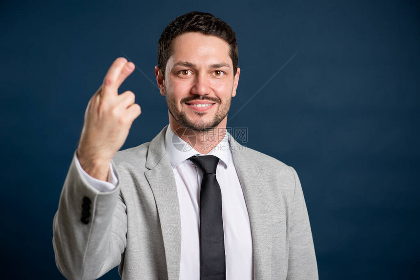 蓝色背景上显示手指交叉手势的商务年轻英俊男肖像图片