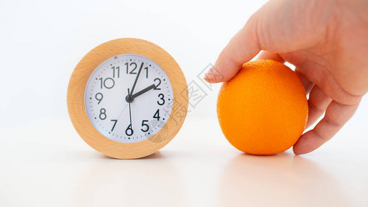 白色桌子背景上的闹钟和橙色水果在手图片