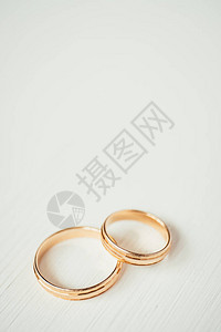 白色木质背景底部的男对环上是女婚礼结霜状的金戒指侧面视图片