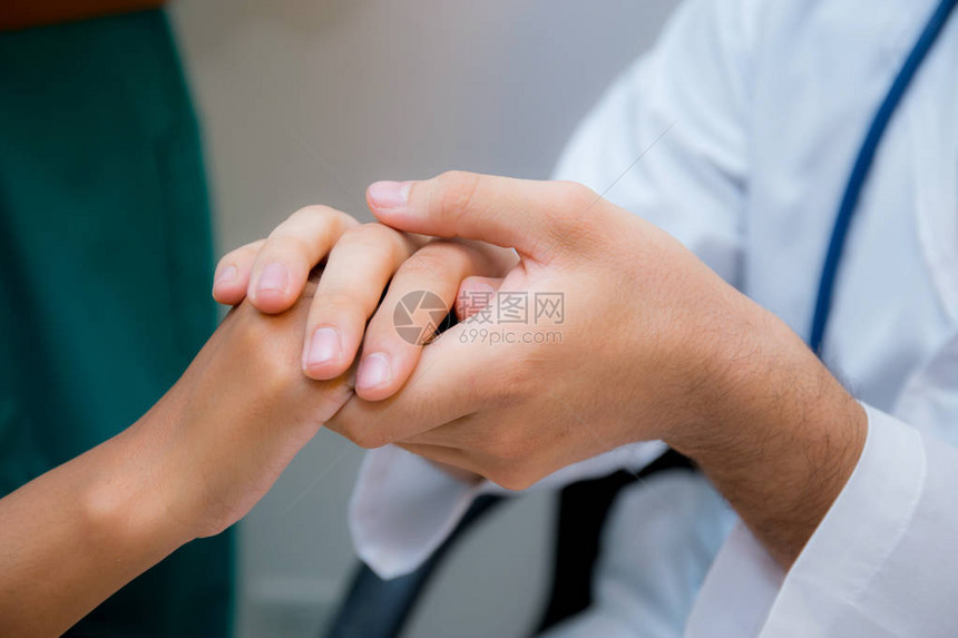 友好的男医生手牵着病人的手坐在办公桌前鼓励同情在体检图片