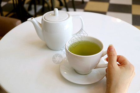 女手握着一杯绿茶在白圆桌上图片