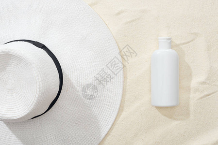 沙滩上白色防晒乳液和草帽的顶视图图片