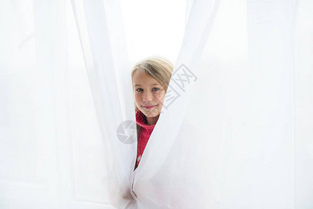 下午躲在窗户后面的白色透明窗帘下的女孩图片