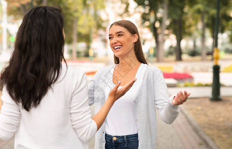 走姿礼仪朋友会议两个快乐的姑娘在公园外门站着聊天和交谈有选择的重背景