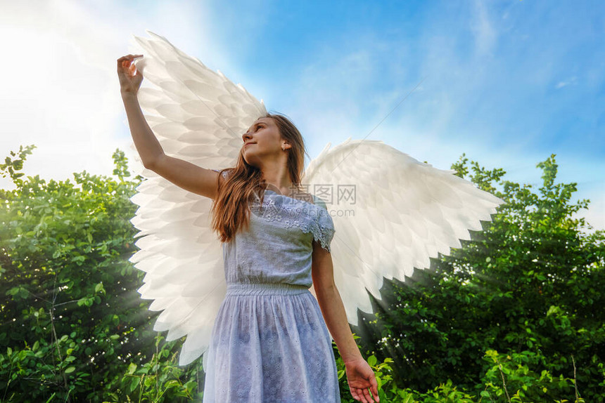 带着天使翅膀和白裙子的可爱幼稚的caucasia女孩穿着蓝色天空背景的白色衣图片