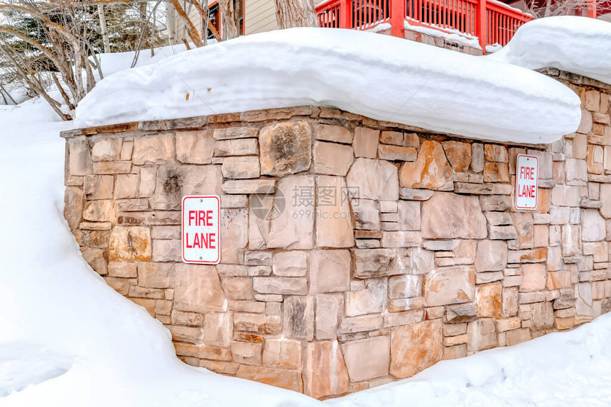 在冬季雪厚的山坡上用火道标志保留石墙的石墙树木和有红阳台护栏的家可以图片