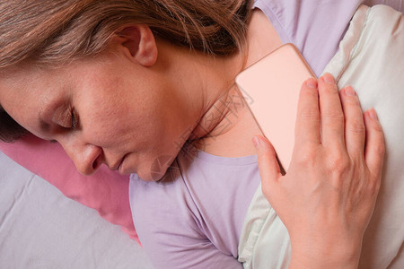 女人在床上用手机睡觉40岁的中年妇女躺在枕头上图片