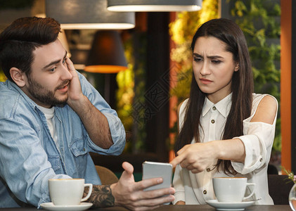 不忠的概念嫉妒的女朋友指着作弊的男朋友电话要求解释坐在自助餐厅背景图片