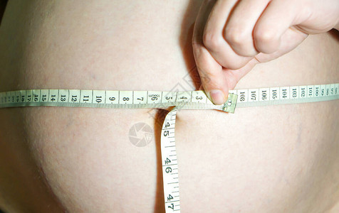 怀孕的女孩用卷尺测量她的胃图片