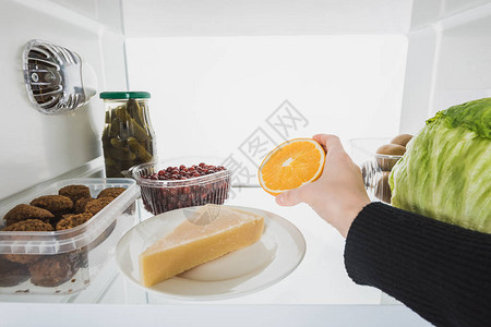 妇女从冰箱中提取橙色切片的割裂式观察图片