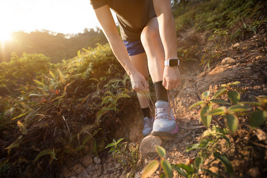 在森林小径上系鞋带的女小道跑者图片
