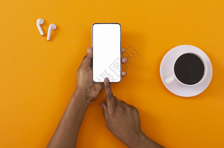 智能手机的音乐应用程序黑色女手用咖啡和无线耳机触摸橙色背景上空图片