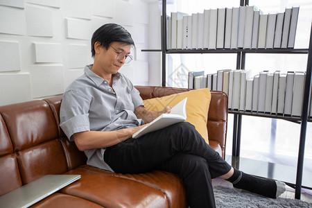 亚裔老人在家中客厅的沙发上读书图片