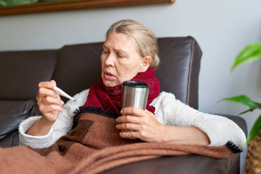 她正在使用温度计患有鼻炎的女人流鼻涕患流感的女人躺在沙发上图片