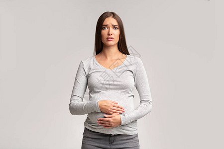 怀孕的妇在灰色背景上忍受痛苦图片
