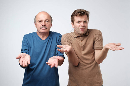 两个成熟的男子的父亲和儿子举起手来表示困惑图片