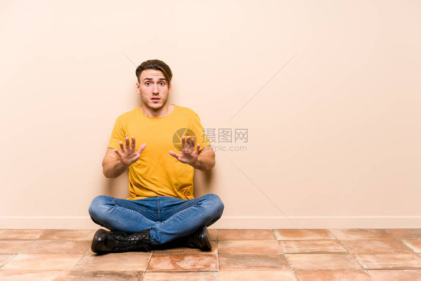 坐在地板上的年轻caucasian男子孤立地拒绝有人表现出令图片