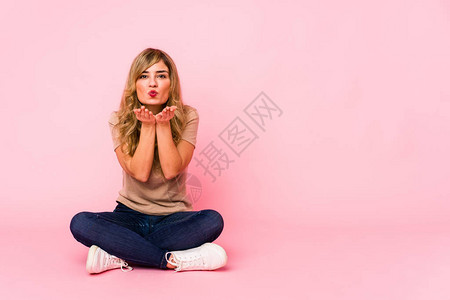 坐在粉红色工作室的金发美女折着嘴唇握着图片