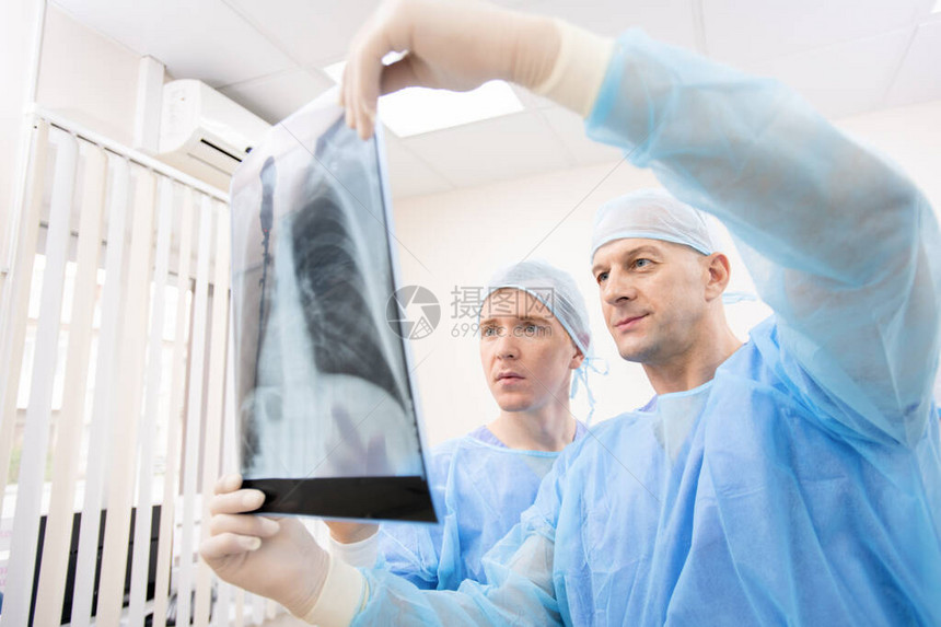 穿制服的年轻和成熟年青医生在医院工作时仔细观察病人肺部X光片图片