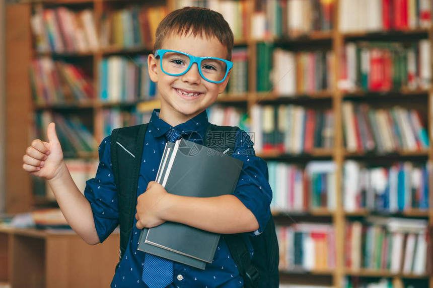 带着蓝色眼镜框领带背包和一摞书的微笑男孩图片