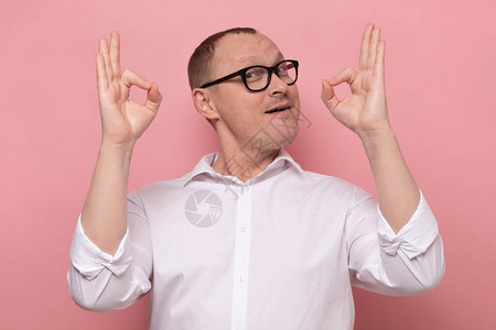 一个快乐的成熟男人的肖像表现不错的手势看着被粉红背景图片