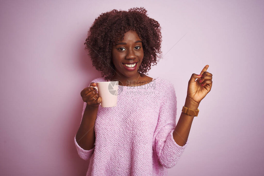 年轻的非洲黑人女端着一杯咖啡站在孤立的粉红色背景上图片