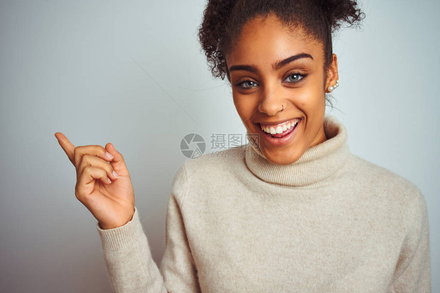在孤立的白色背景上穿着冬季高领毛衣的非洲裔美国女非常高兴地用手和图片