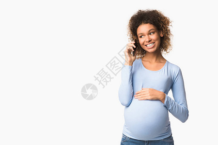 非洲裔美籍孕妇用手机和触摸肚子站在白色背景空闲间上交谈的非图片