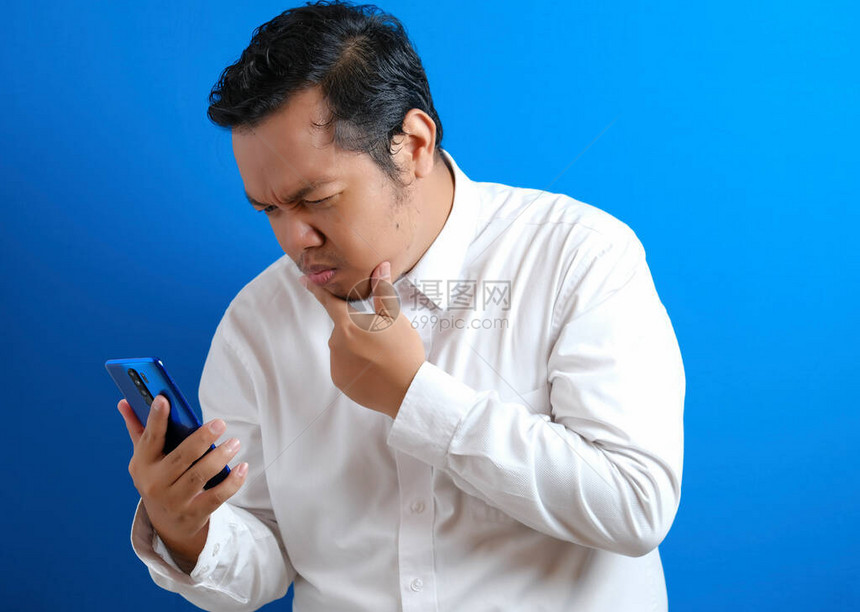 身穿休闲白衬衫试图用智能手机仔细阅读新闻好奇的面部表情的亚洲年图片