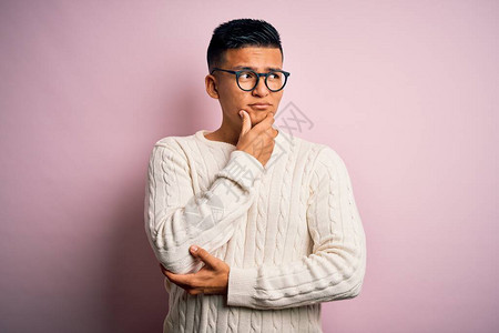 年轻英俊的拉丁男子穿着白色休闲毛衣和粉红色背景的眼镜图片