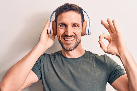 年轻英俊的男人用耳机在孤立的白色背景上听音乐图片