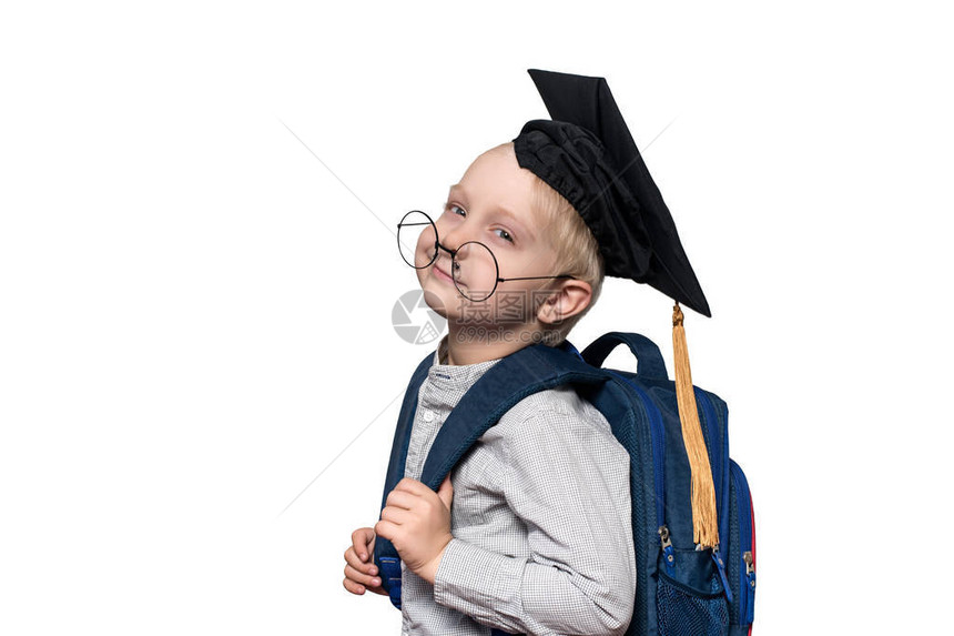 一个戴着眼镜学术帽子和书包的累金发男孩的肖图片