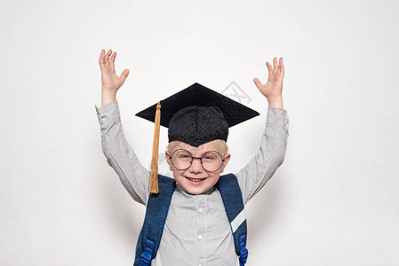 一个戴着大眼镜学术帽子和背包的金发男孩的喜悦肖像图片