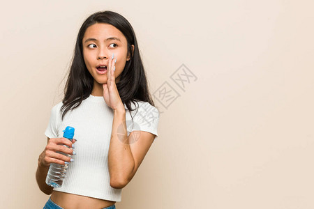 拿着水瓶的年轻亚洲女人正在说一个秘密热辣的新闻图片