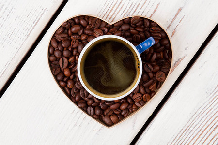 一杯咖啡站在由咖啡粒制成的心上咖啡爱情观白图片
