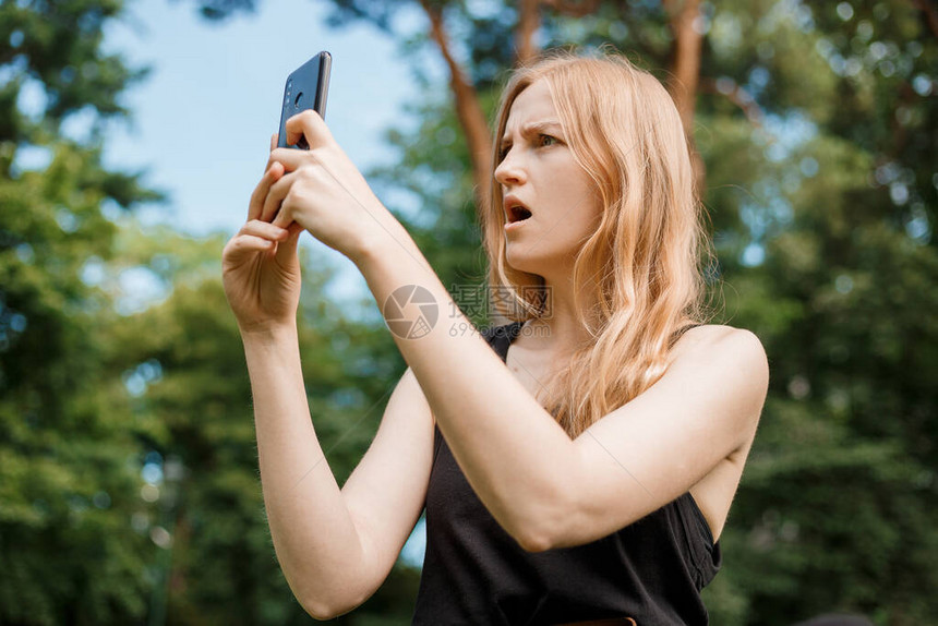 金发碧眼的年轻时髦女人在公园里使用手机不满意旅行和积图片