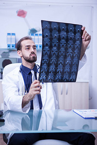 诊所柜子里的年轻医生拿着脑部X光片医生检查病图片