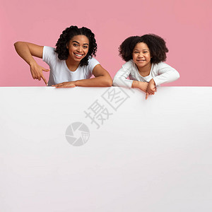 欢乐的非洲母亲和女儿在粉红背景上的白广告委员会上倾斜图片