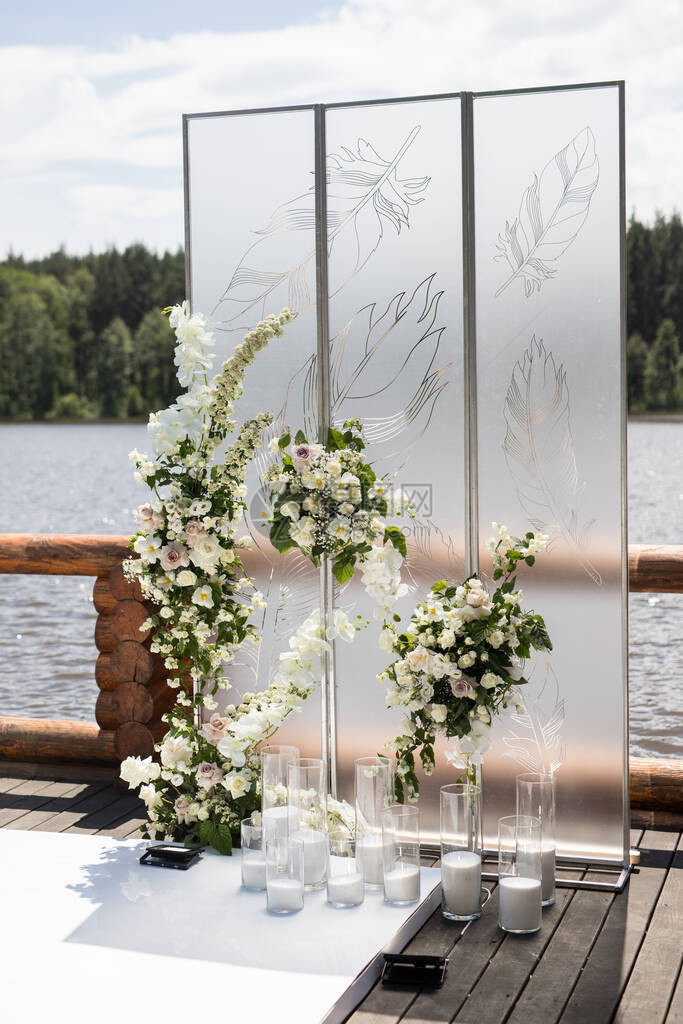 婚礼的垂直照片与白色透明屏幕和鲜花和蜡烛带羽毛和白玫瑰的两个屏风的图片