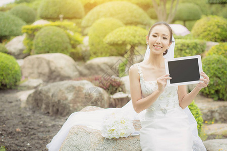亚洲的新娘持有并展示数字平板电脑图片