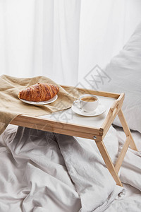 咖啡和羊角面包用枕头放在白床图片