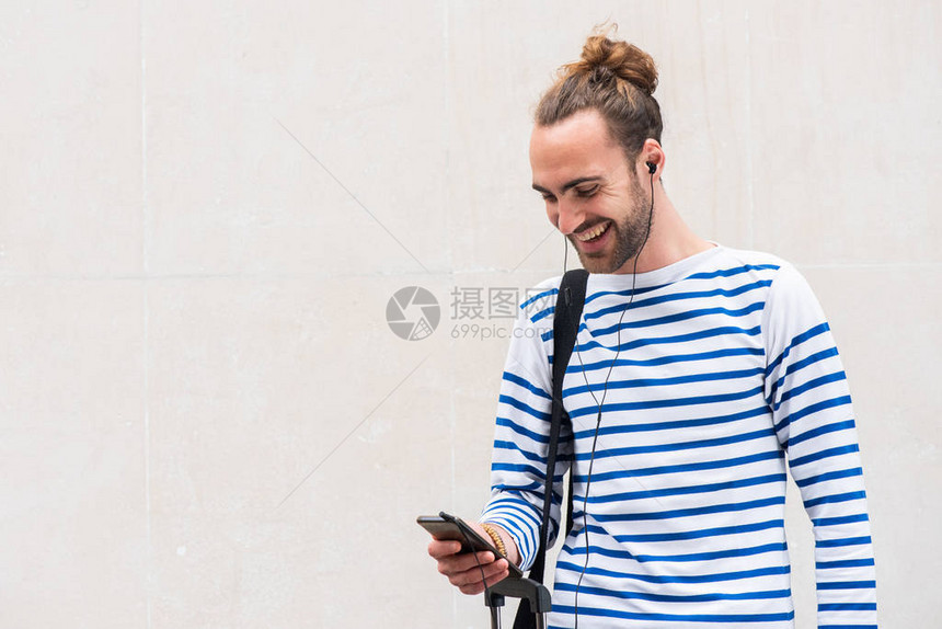 快乐的年轻人一边看手机一边用白色背景的耳机图片