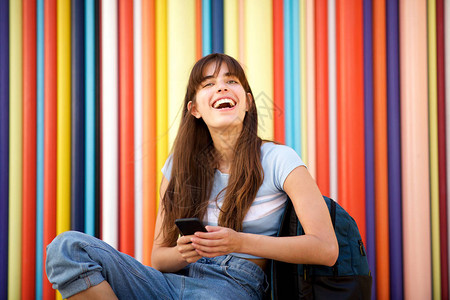 年轻女笑的肖像与手机和包袋坐图片