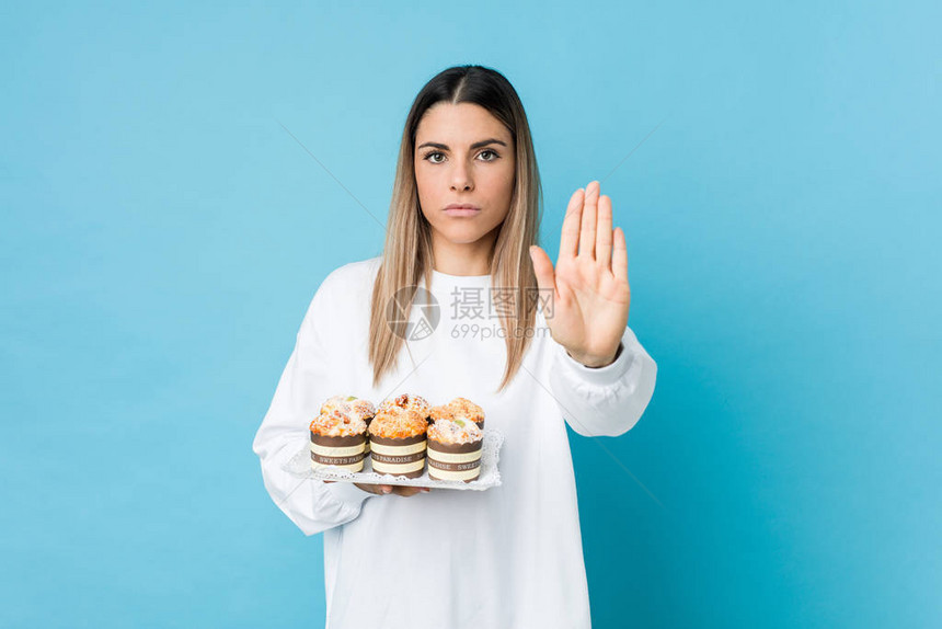 年轻caucasian女人拿着甜点蛋糕站在伸展的手外显示停图片